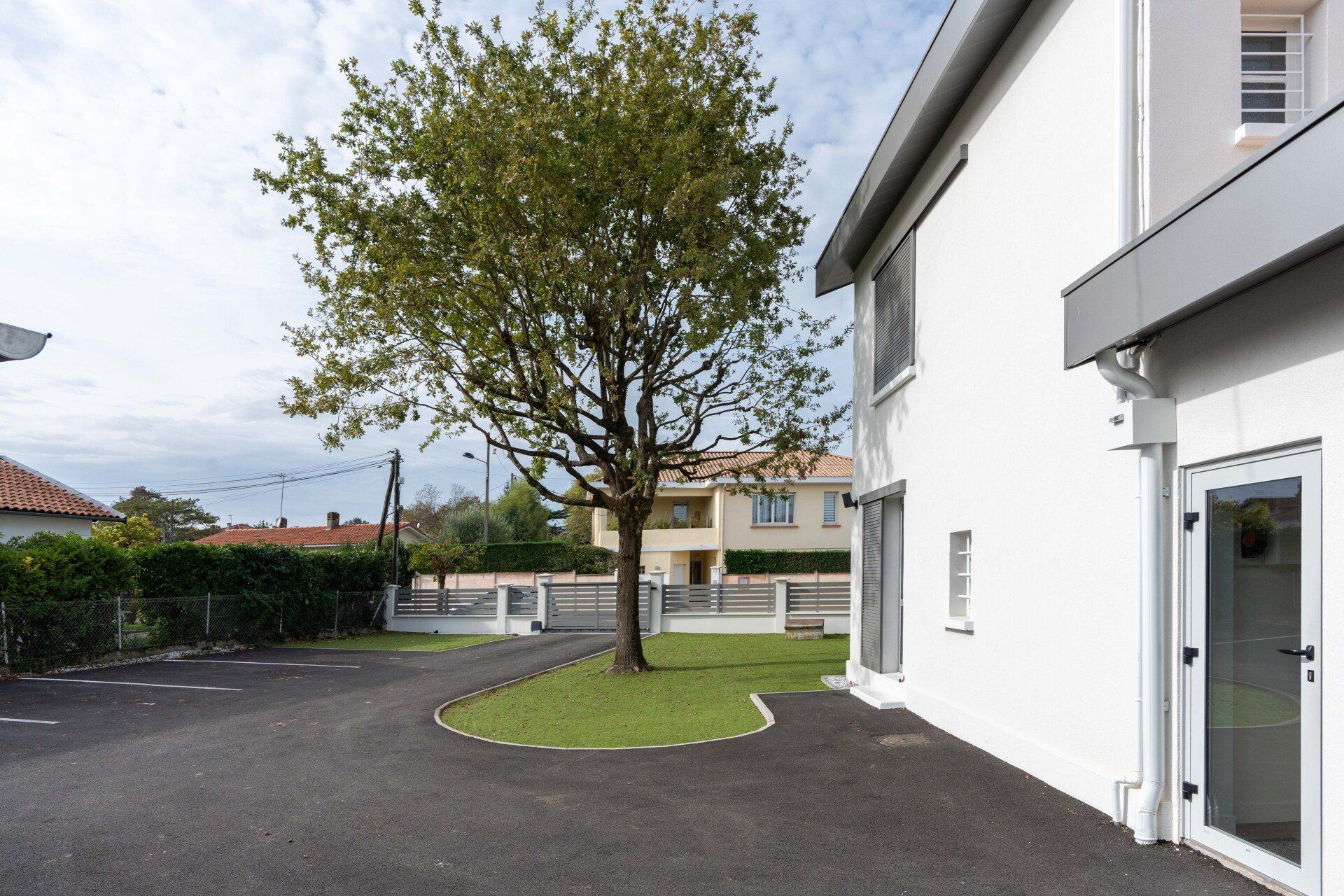 Extérieur d'une maison moderne avec un arbre, une allée et une petite pelouse dans une cour pavée