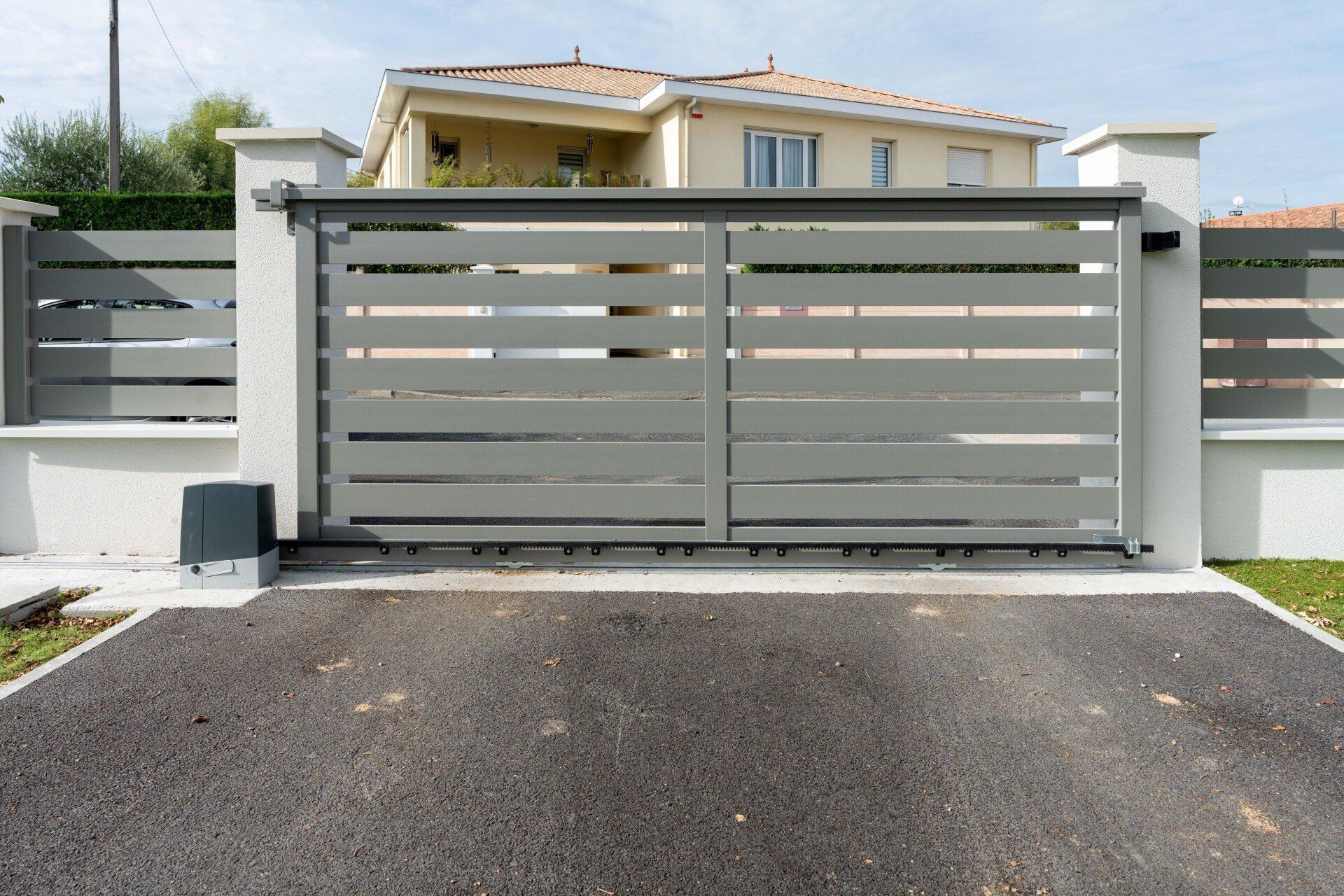 Portail d'allée moderne en métal gris devant une maison avec une allée pavée.