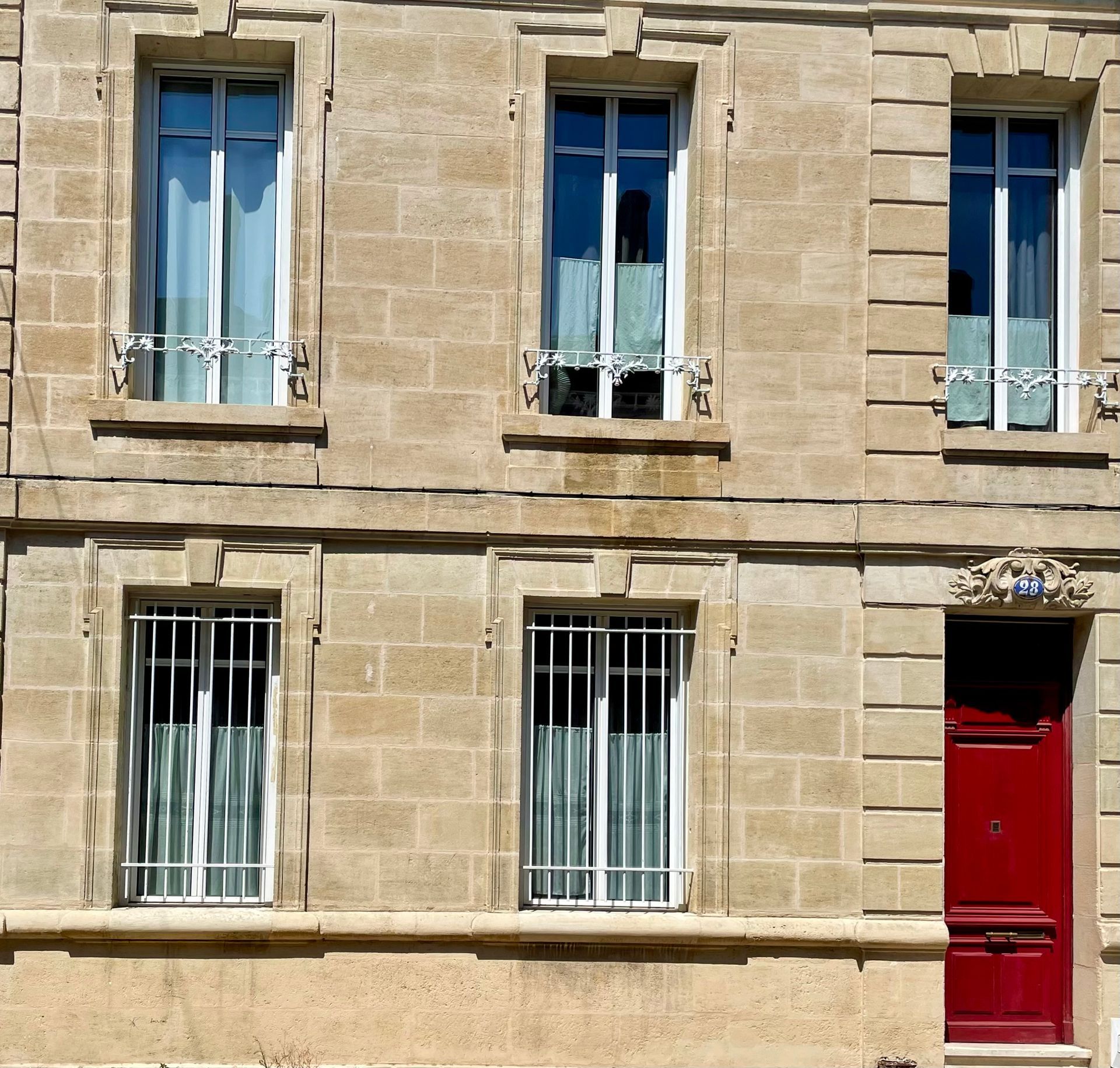 Façade en pierre avec trois fenêtres et une porte rouge vif
