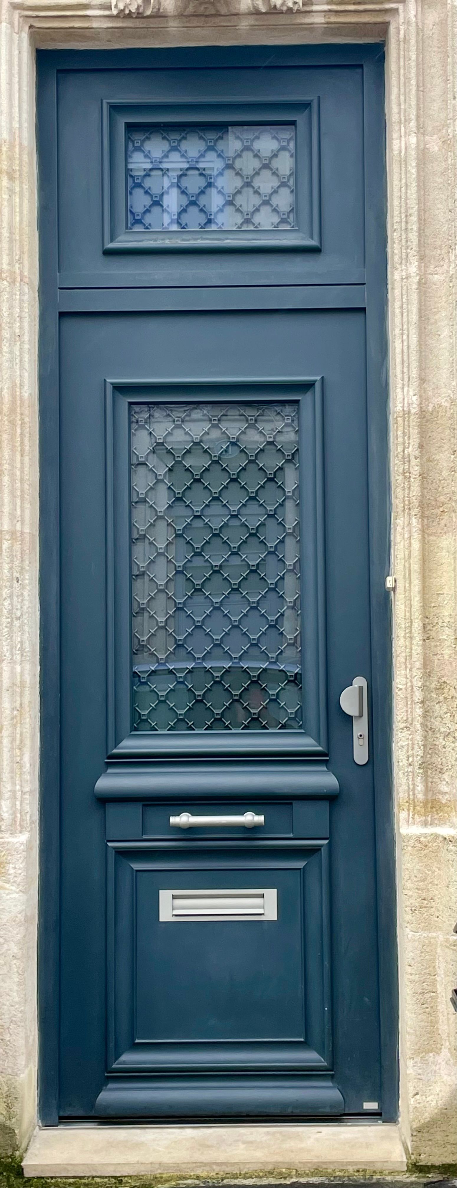 Porte à panneaux bleus avec fenêtre en verre dépoli et fente à lettres dans une entrée en pierre