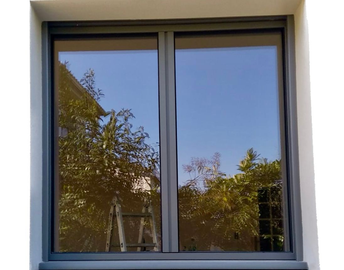 Fenêtre fermée laissant apparaître des arbres et un ciel bleu sur un mur blanc