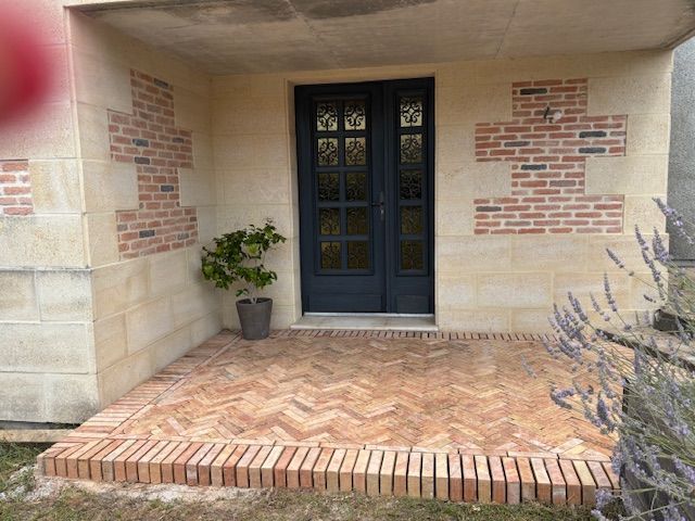 Porche d'entrée en briques avec double porte vitrée, plante en pot et marches en briques menant à l'entrée