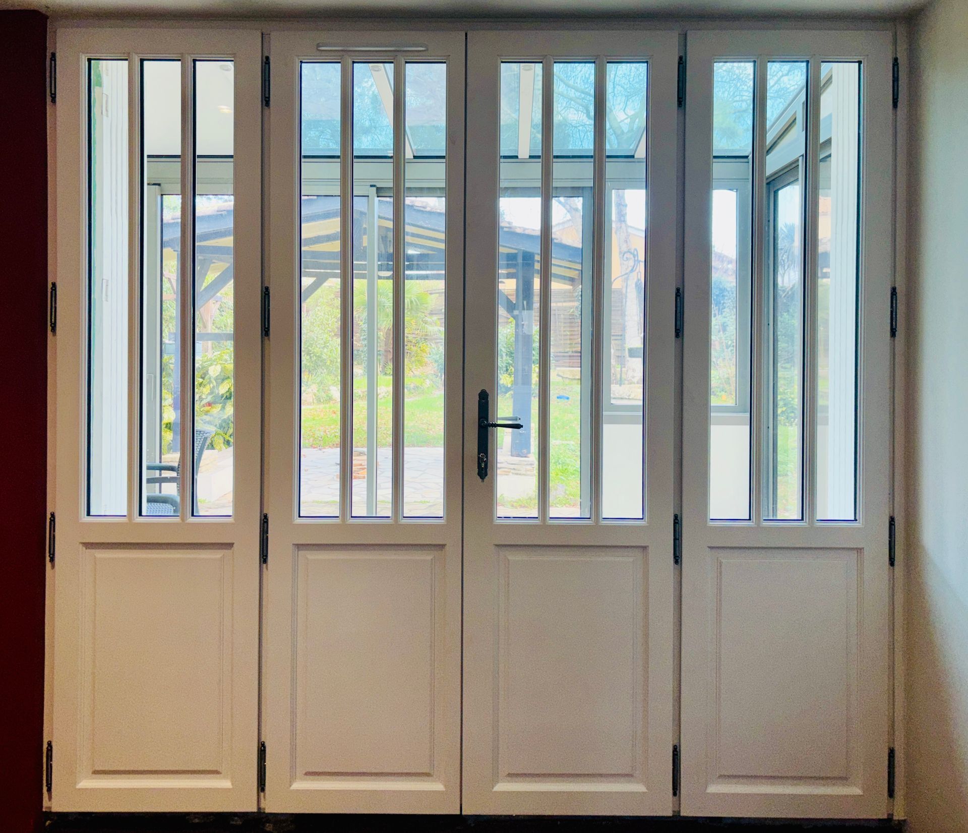 Double porte vitrée blanche à barreaux verticaux donnant sur une vue extérieure lumineuse
