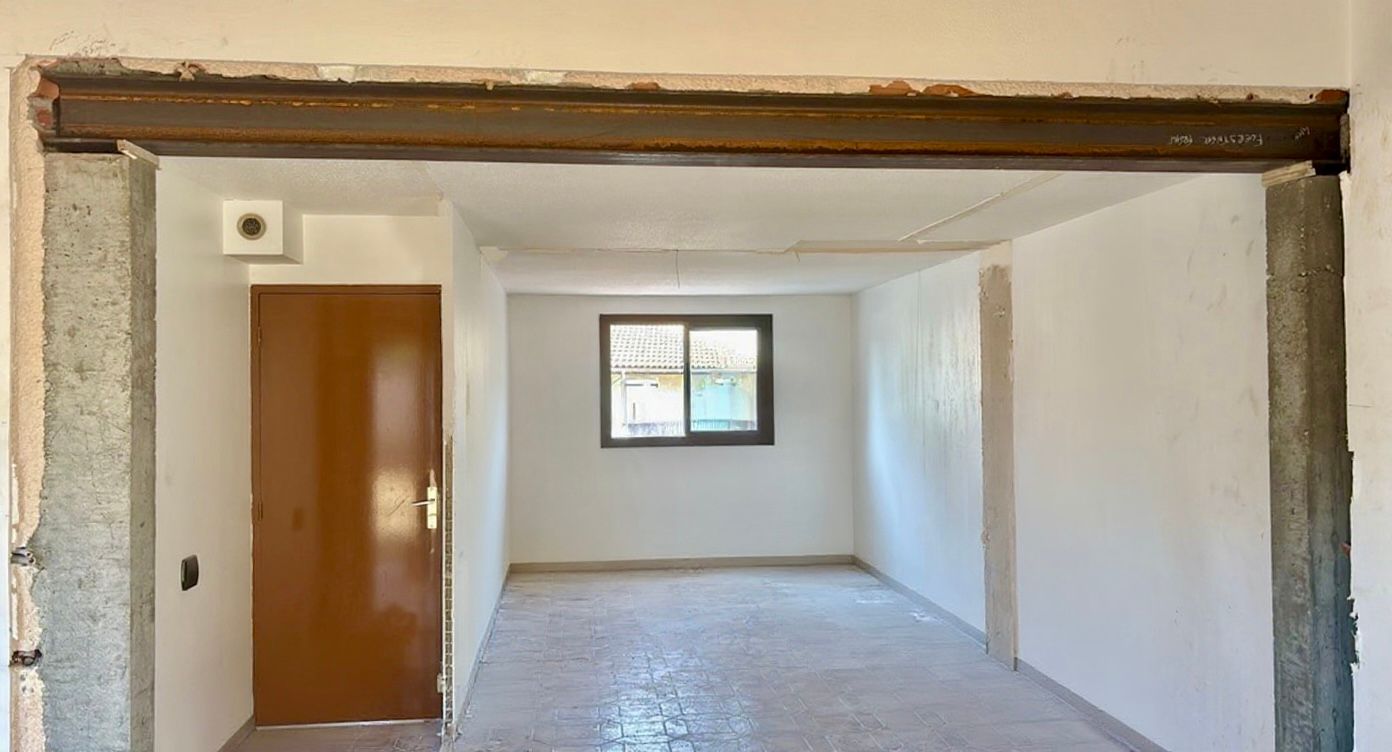 Pièce vide et inachevée avec des murs blancs, une porte en bois et une petite fenêtre