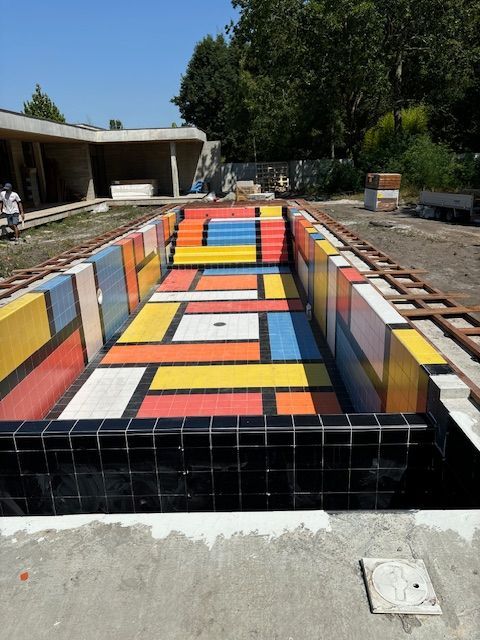 Bassin de fontaine rectangulaire carrelé et coloré dans une cour, avec des bordures noires et des motifs géométriques lumineux.