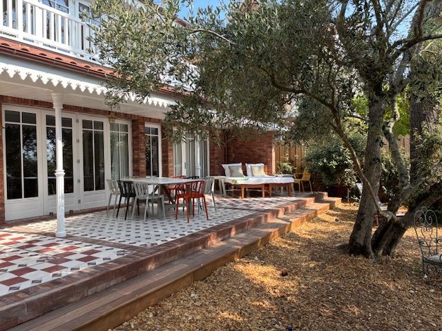 Terrasse extérieure avec tables et chaises à côté d'un bâtiment blanc et d'arbres dans un jardin ombragé