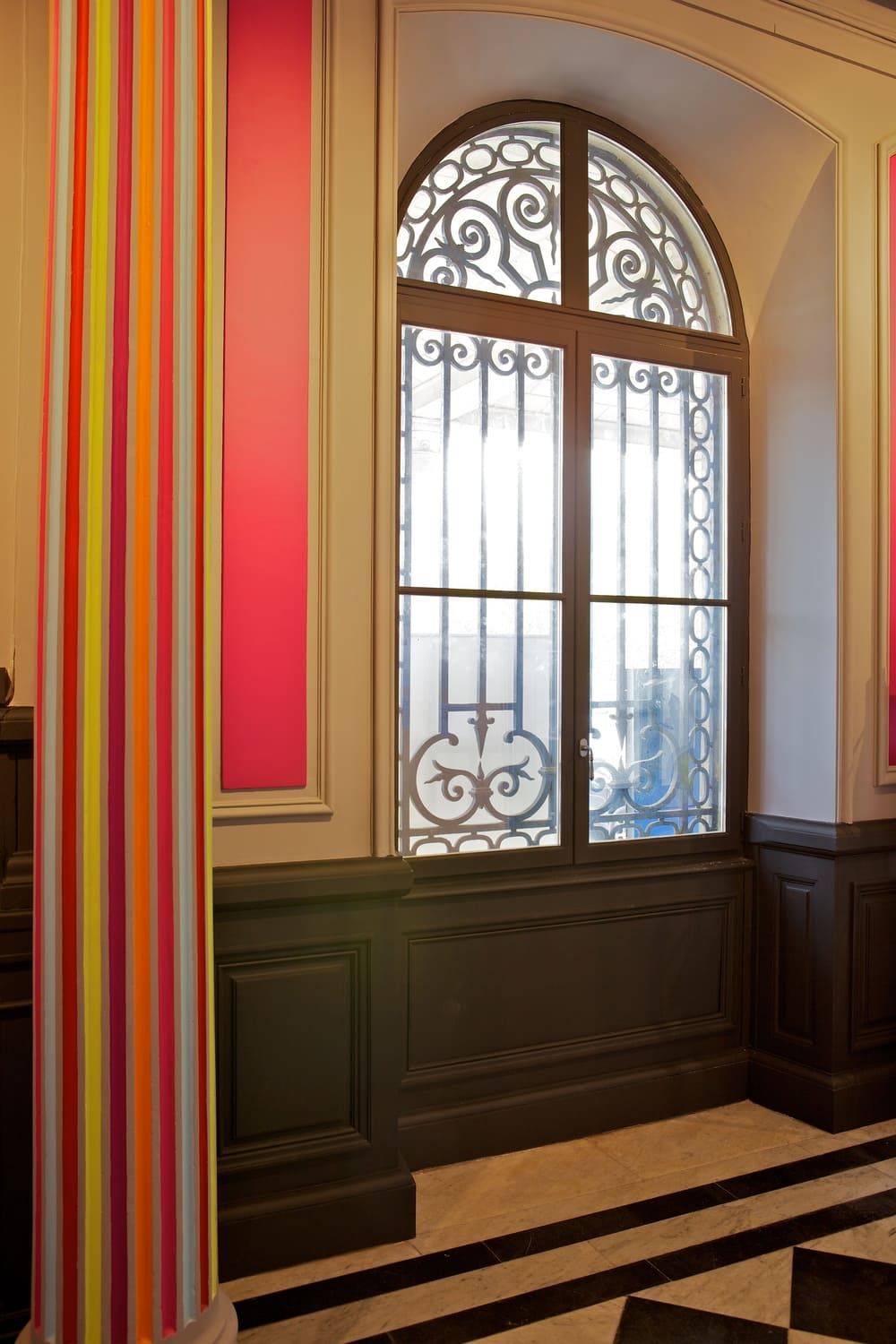 Fenêtre cintrée ornée de ferronnerie décorative dans un couloir intérieur coloré