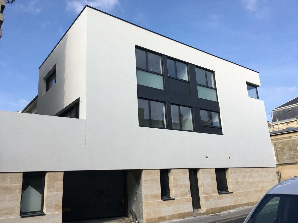 Bâtiment moderne blanc et noir avec de grandes fenêtres et un socle en pierre sous un ciel bleu