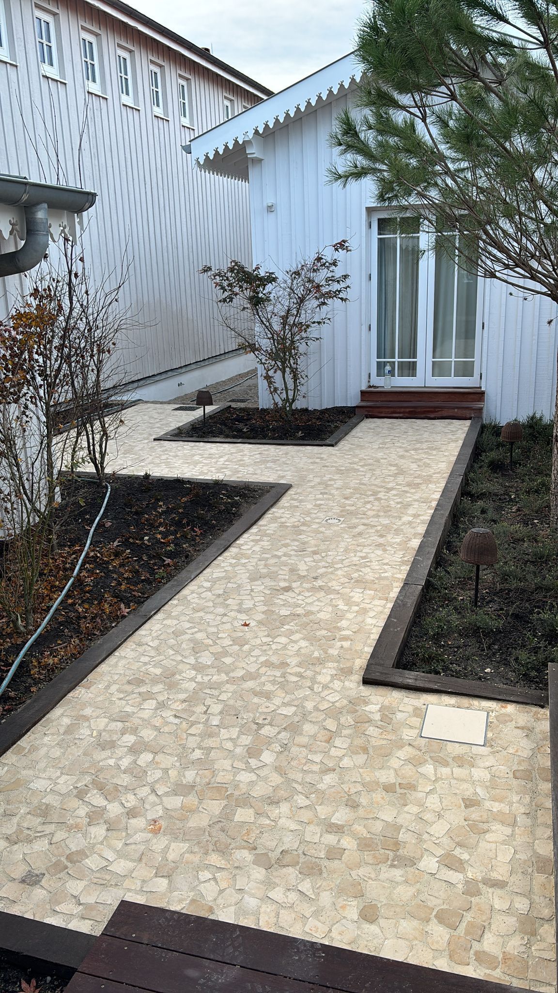Allée en pierre menant à une porte d'entrée bordée d'un revêtement blanc et de parterres de fleurs aménagés