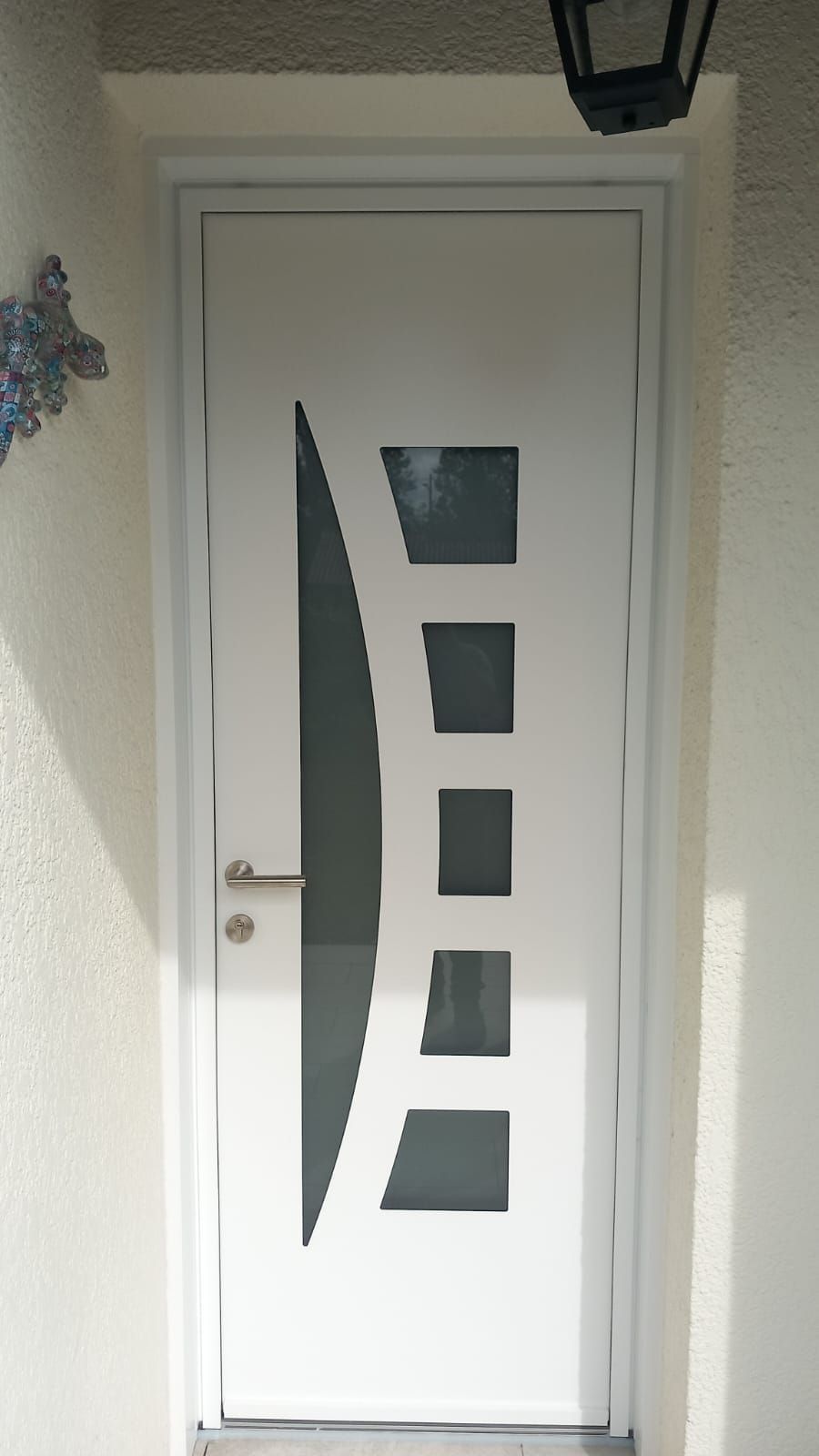 Porte d'entrée blanche avec panneaux de verre dépoli incurvés et poignée argentée sous un petit porche