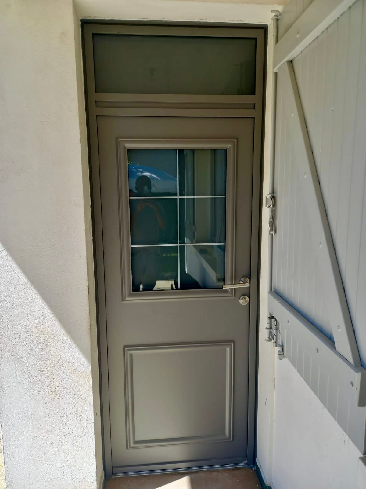 Porte blanche fermée avec une petite fenêtre, située dans une entrée extérieure étroite aux murs clairs.