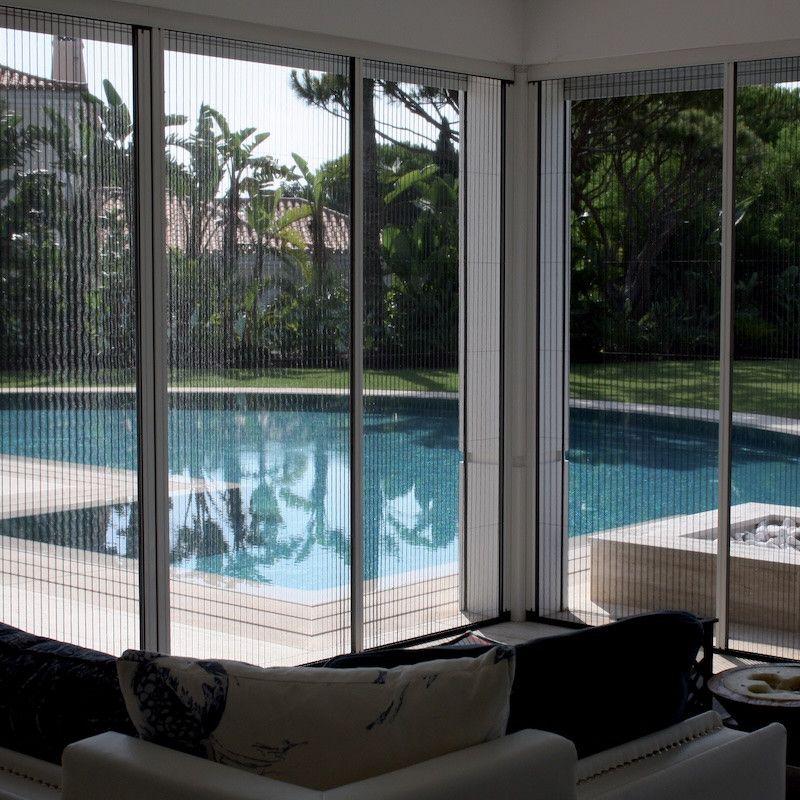 Terrasse couverte avec canapés donnant sur une piscine bleue et des arbres tropicaux dans le jardin.