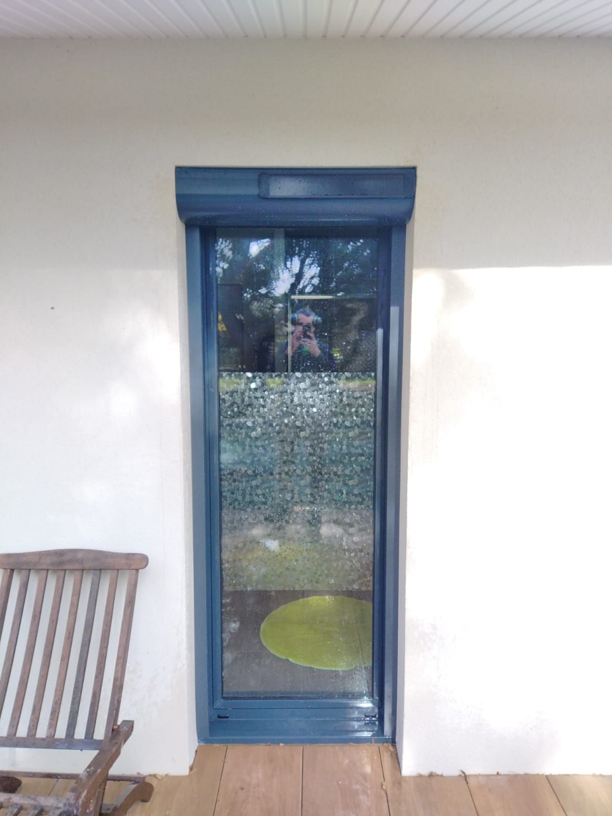 Porte vitrée étroite à cadre bleu dans un mur blanc, avec une chaise en bois partiellement visible sur la gauche.