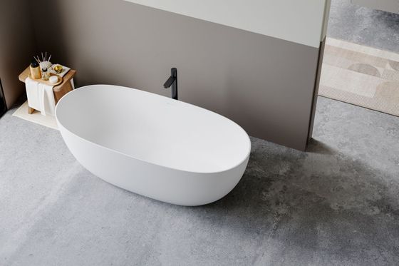 Salle de bains moderne avec baignoire ovale blanche, robinet noir et petite table d'appoint sur un sol gris.