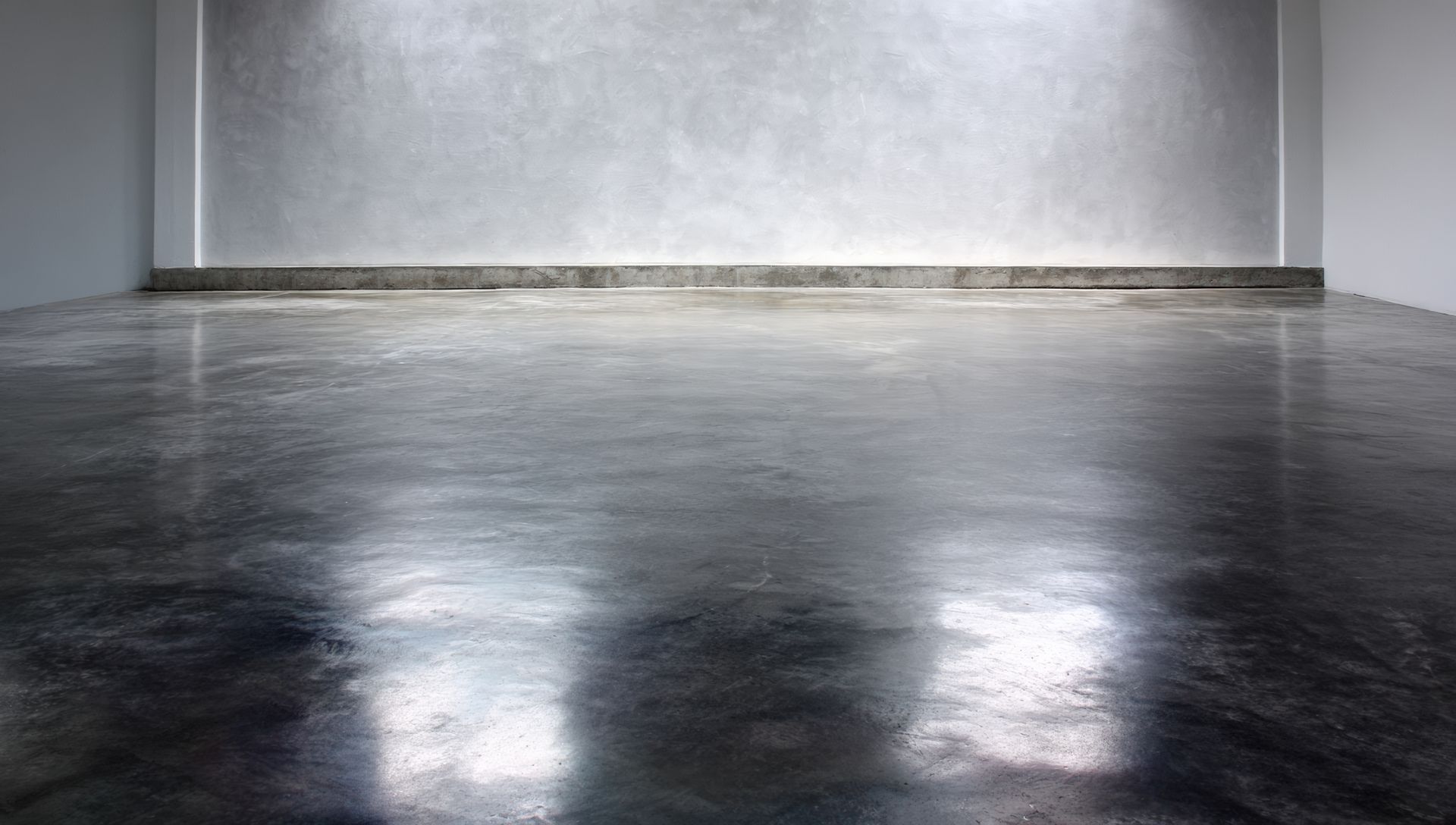Pièce grise vide avec un sol sombre et le reflet de deux lumières vives.