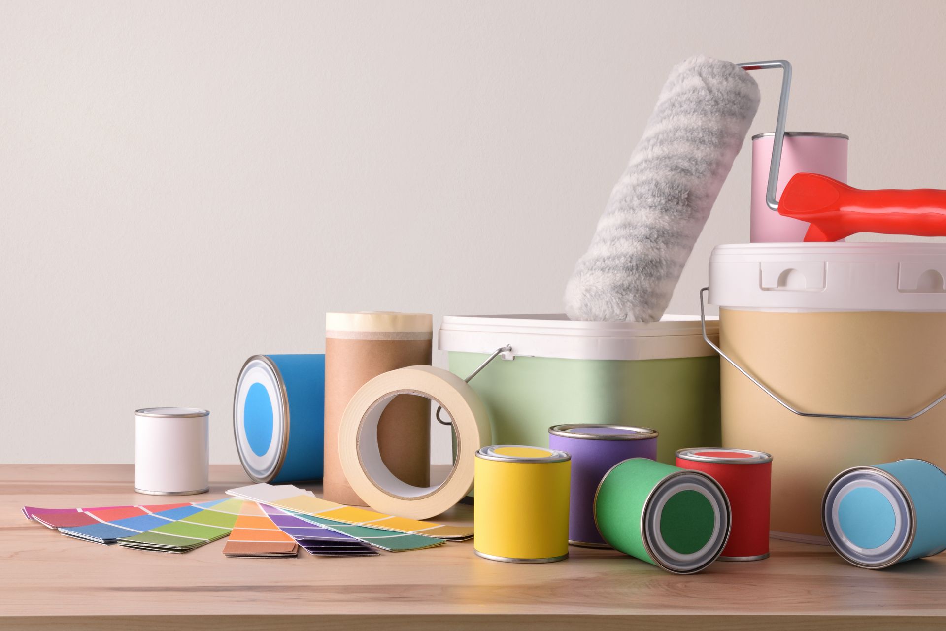 Des rouleaux de ruban adhésif coloré, des pots de peinture et du matériel de peinture posés sur une table en bois.