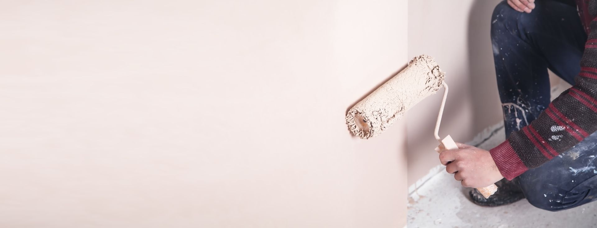 Une personne vêtue d'une chemise éclaboussée de peinture peint un mur en blanc avec un rouleau.