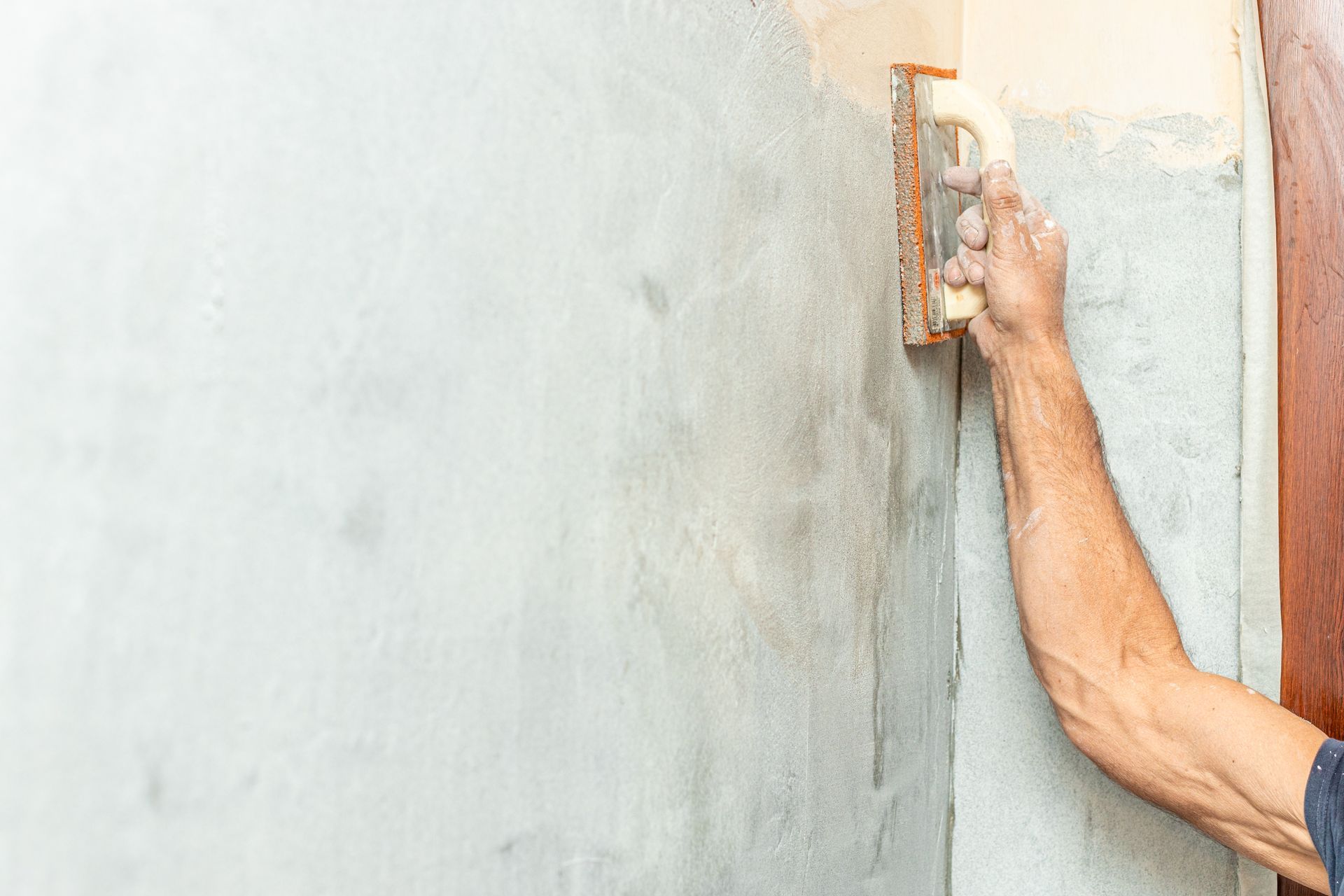 Une personne lisse du plâtre sur un mur à l'aide d'une truelle.