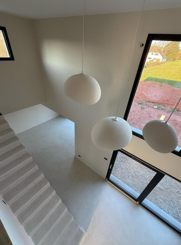 Intérieur de la cage d'escalier avec murs blancs, suspensions lumineuses en forme de globe et une grande fenêtre inclinée.