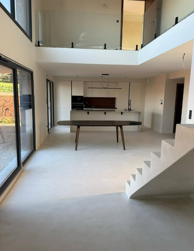 Salon moderne ouvert avec cuisine, escalier blanc et grandes baies coulissantes .