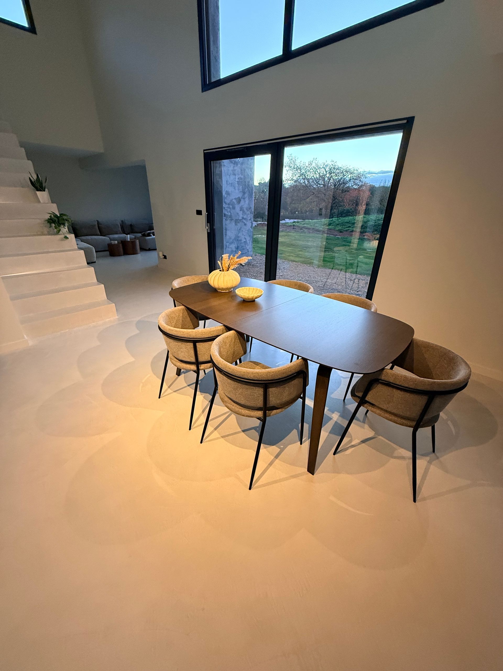 Salon moderne ouvert avec cuisine, escalier blanc et grandes baies coulissantes .