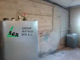 Tanque de agua plateado con logo “ser” y tuberías en un cuarto de servicio.