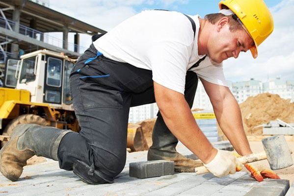 Obrero de la construcción con mono y casco colocando ladrillos al aire libre.