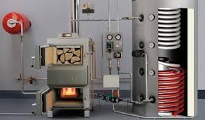 Horno de leña conectado a un acumulador de agua caliente. Horno encendido con leña en su interior; tubos rojos enrollados visibles.