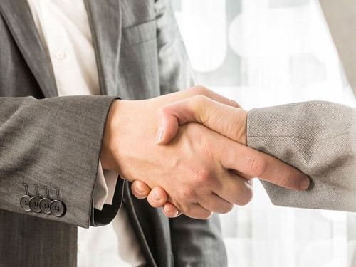 Dos personas de traje se dan la mano, lo que significa un acuerdo o trato.