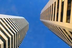 Dos rascacielos altos y blancos contra un cielo azul brillante, vistos desde un ángulo bajo.