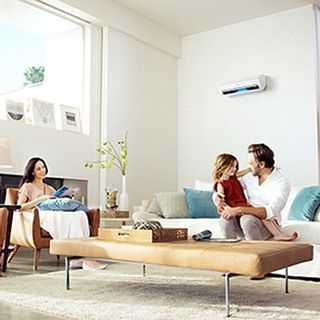 Familia en una sala luminosa con aire acondicionado. Mujer a la izquierda, hombre con un niño en brazos, sofá a la derecha.