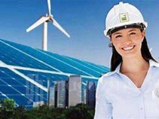 Una mujer con casco sonríe, con paneles solares y turbinas eólicas en el fondo.