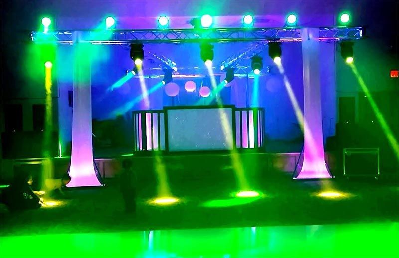 Un escenario con luces de colores, focos y una cabina de DJ.