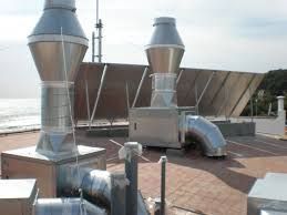 Sistema de ventilación industrial en azotea con conductos y chimeneas de extracción plateados, con una playa como telón de fondo.