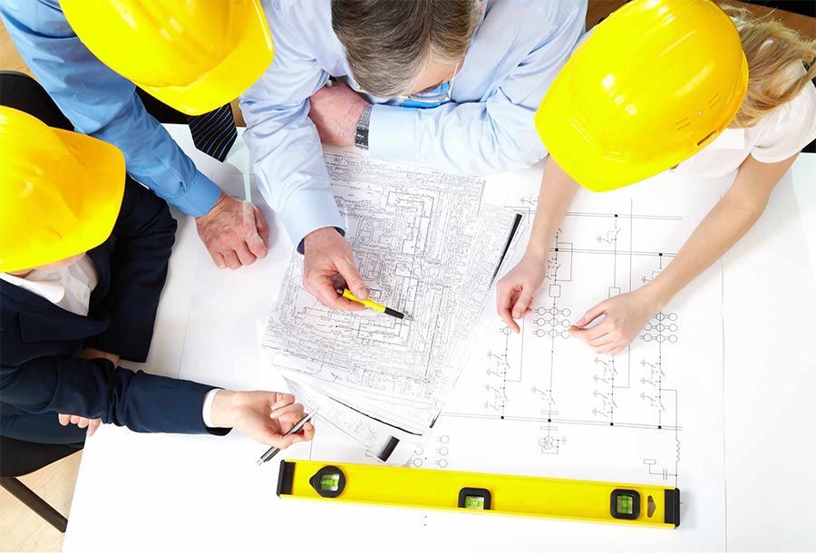 Cuatro personas con casco revisan planos sobre una mesa blanca. Hay un nivel y un bolígrafo.