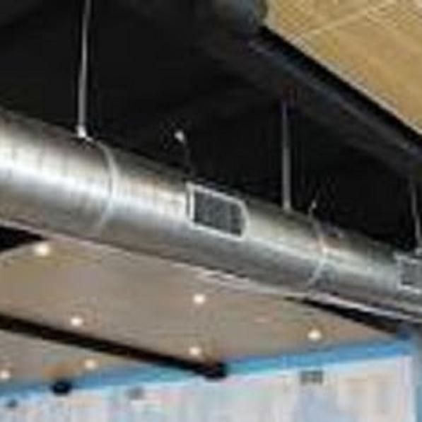 Conductos de HVAC plateados suspendidos de un techo negro con luces empotradas y un panel de color claro.