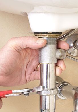 Mano usando una llave para apretar la plomería debajo de un fregadero blanco.