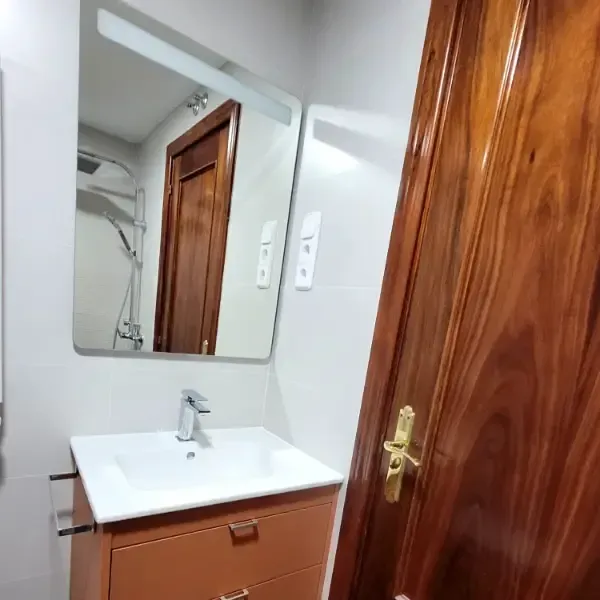 Baño con tocador marrón, lavabo cuadrado, espejo grande y puerta marrón.