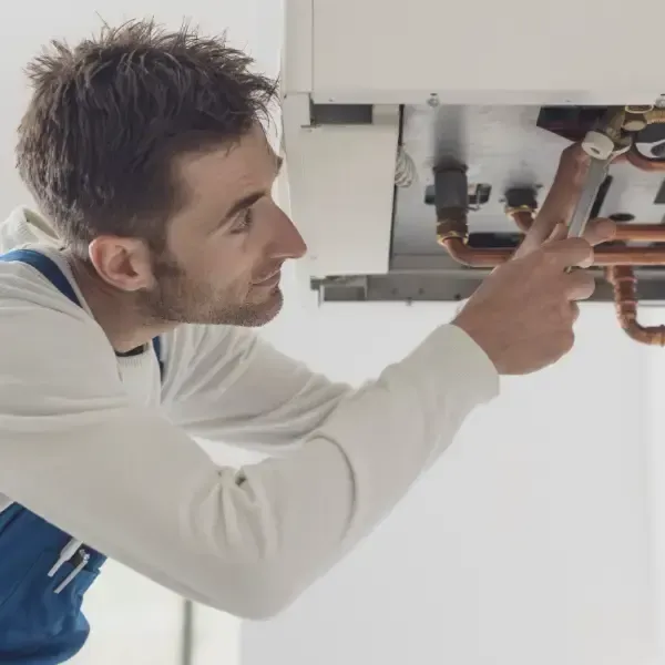 Fontanero inspeccionando una caldera. Vestido de azul y camisa blanca. Trabajaba en un espacio cerrado.