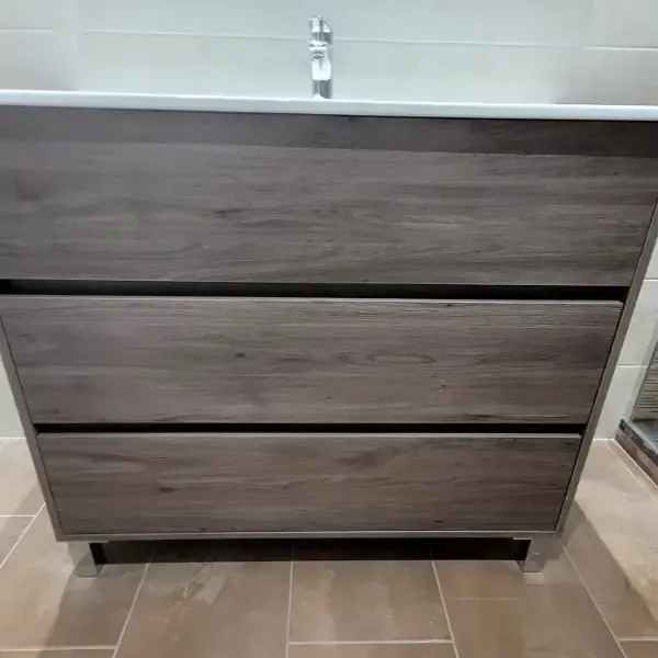 Mueble de baño de madera con tres cajones y encimera en color blanco.