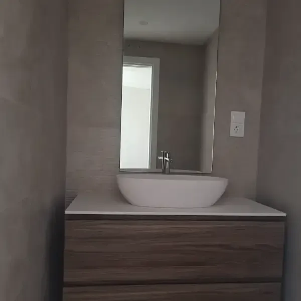 Baño con tocador flotante de madera, lavabo blanco, espejo rectangular y paredes gris claro.