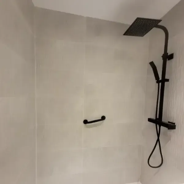 Artefactos de ducha de color negro sobre pared de azulejos de color gris claro; pasamanos.