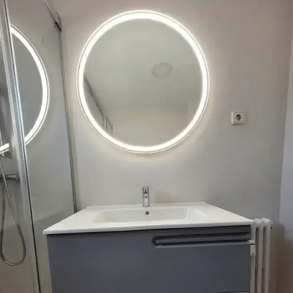Mueble de baño con mueble gris, lavabo blanco y espejo redondo con iluminación LED.