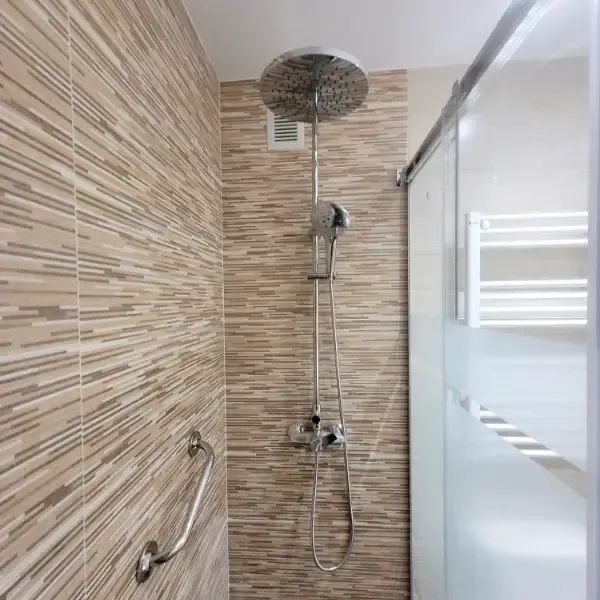 Ducha con cabezal de lluvia, ducha de mano y puerta corrediza de cristal; azulejos beige y blancos.
