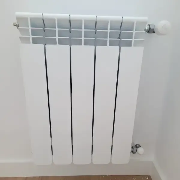Radiador blanco moderno montado en la pared. Tiene barras verticales y una válvula en el lado derecho.