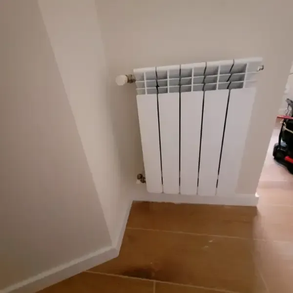 Radiador blanco en pared, montado sobre suelo de madera.