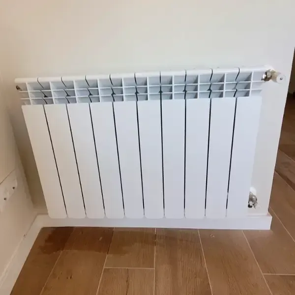 Radiador de aluminio blanco montado en una pared beige sobre un suelo de baldosas.