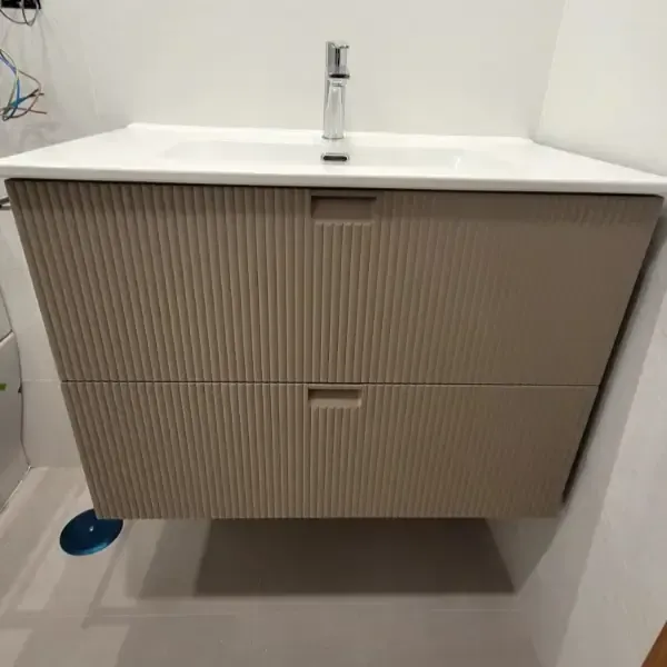Mueble de baño color tostado con dos cajones y encimera blanca con grifería plateada.