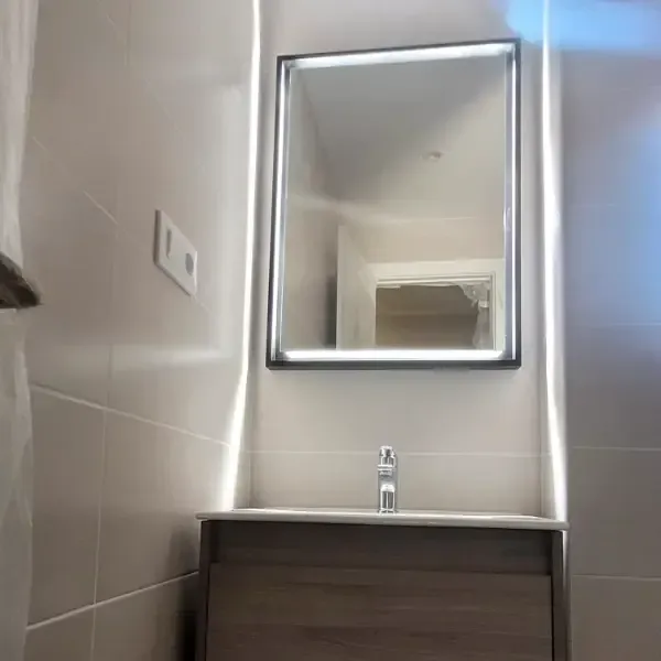 Baño con espejo iluminado encima de lavabo y mueble.