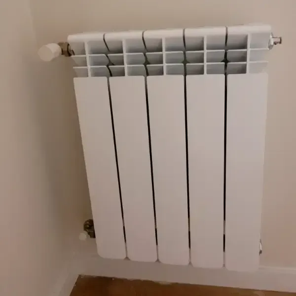 Radiador de aluminio blanco montado en una pared beige en una esquina.